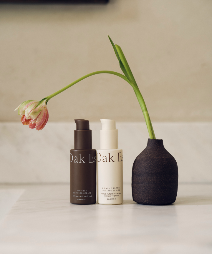 Two skincare products and a black vase with a tulip on a light surface.