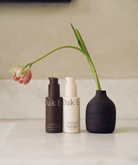 Two skincare products and a black vase with a tulip on a light surface.